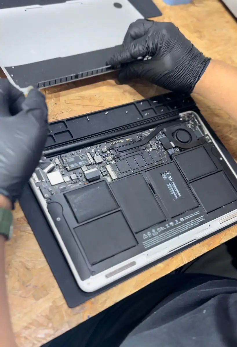 MacBook aberto na bancada, com a tampa inferior removida e a bateria e a placa à vista.
