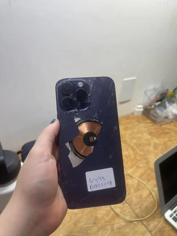 O mesmo iPhone 14 Pro Max roxo antes, com a tampa traseira estilhaçada e a bobina exposta.